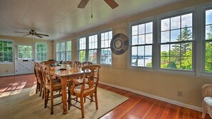 A dining room with a wooden table and chairs, large windows, and a ceiling fan.