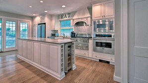 A spacious kitchen with white cabinetry, a large island, stainless steel appliances, and a view through the windows.