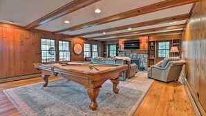 A spacious room with a pool table, a comfortable armchair, and a stone fireplace.