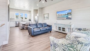 A spacious living room with a blue leather sofa, a patterned armchair, and a dining area with a white table and chairs. - Ahoy Matey Sp151 4 Bedroom Home by RedAwning (Fulton)
