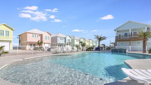 A swimming pool with a white deck and lounge chairs, surrounded by colorful houses with balconies and a clear blue sky.