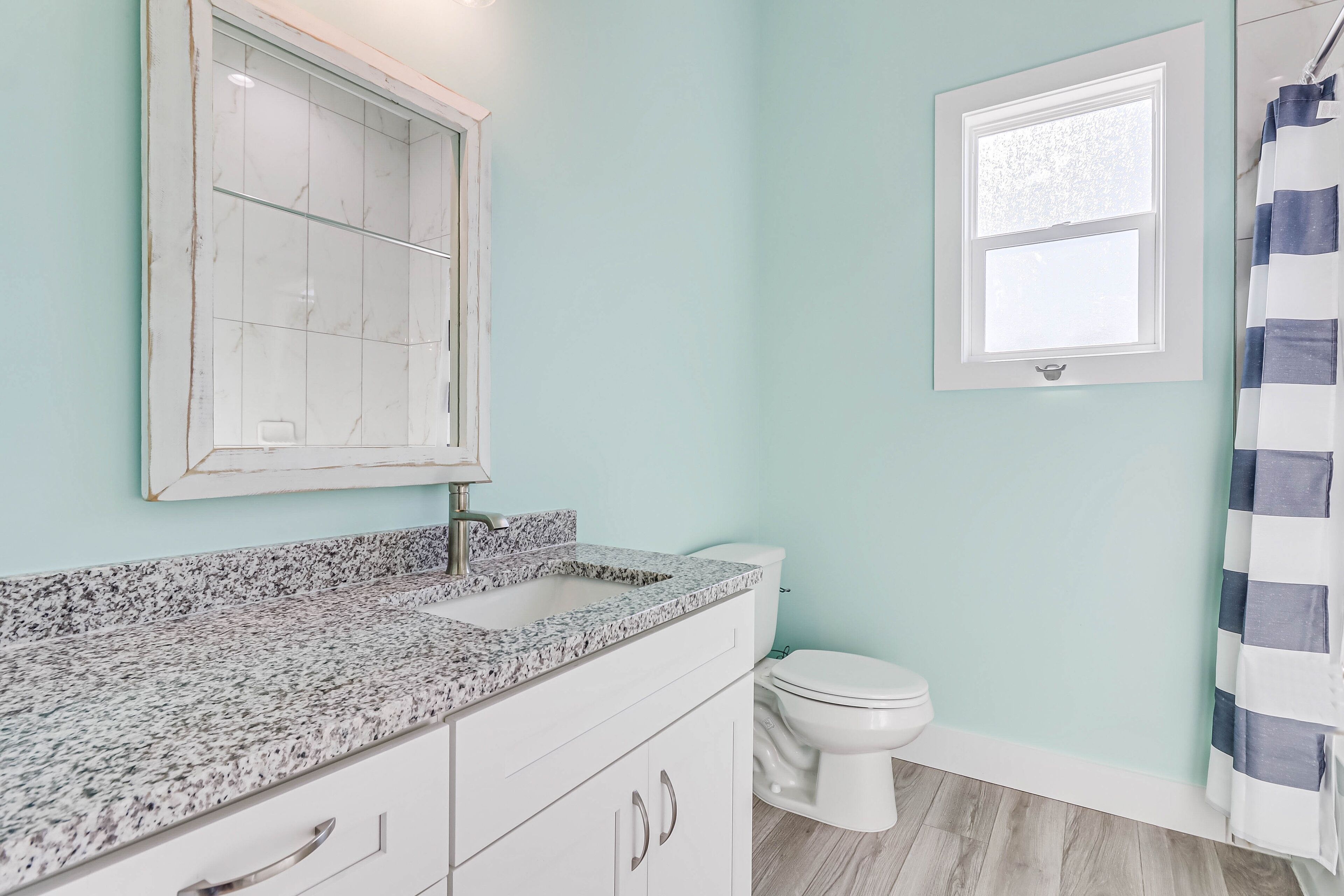 A bathroom with a white toilet, a sink with a granite countertop, and a shower curtain.