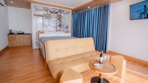 A modern hotel room with a sofa bed, a small wooden table with a bottle and glasses, a decorative wall panel, and a painting on the wall. - Resort Đá Bàng Homestay & Restaurant (Ho Chi Minh City)