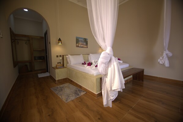 A bedroom with a canopy bed, wooden flooring, a bench, and a painting on the wall. - Mafia dream hotel (Mafia Island)