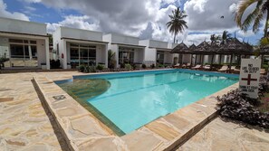 Una piscina con un cartel que indica que no hay salvavidas de servicio, rodeada de palmeras y sillas de descanso.