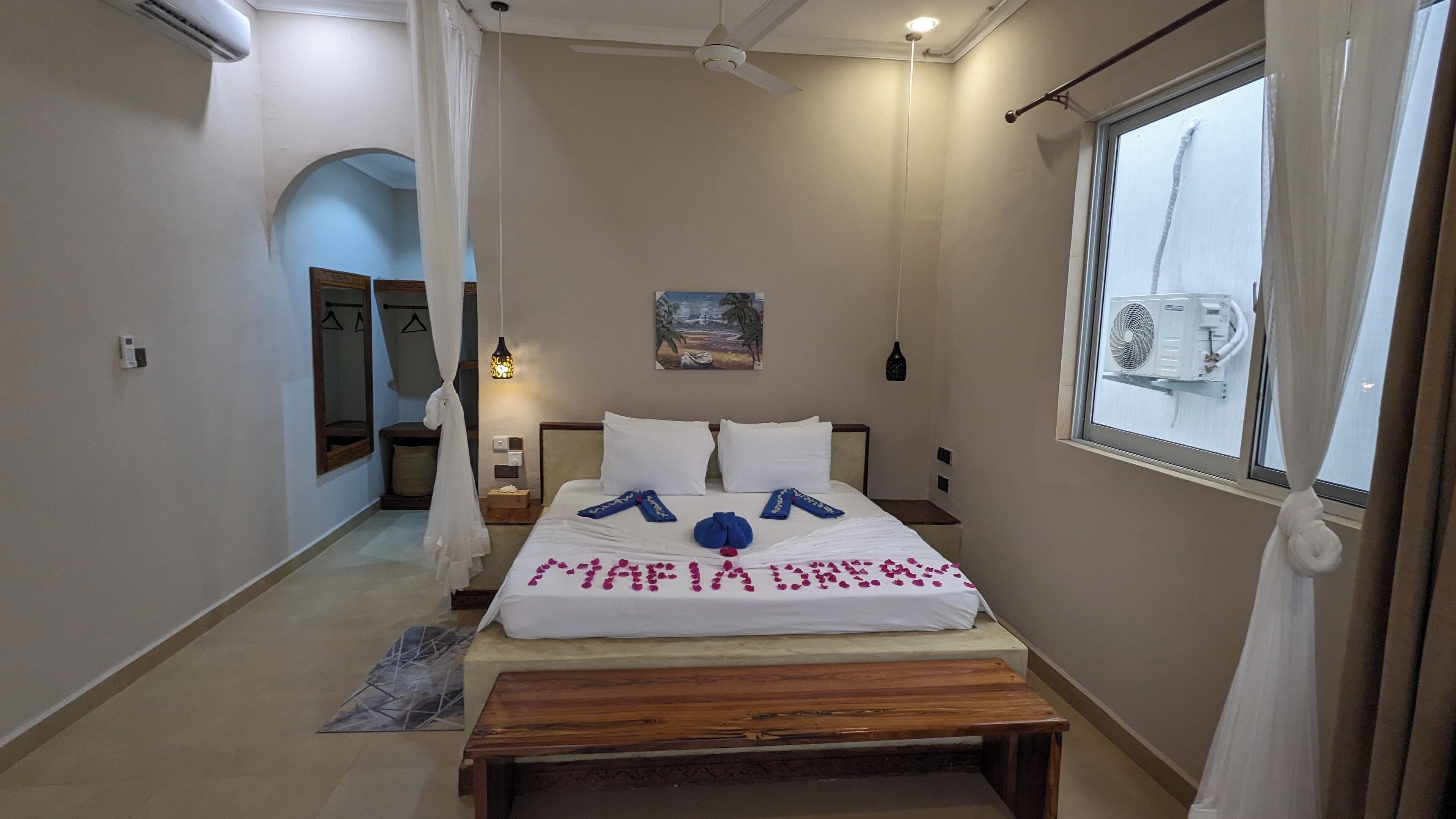 Habitación de hotel con cama, mesitas de noche, un banco, una ventana y un ventilador de techo.