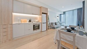 A modern kitchen with integrated appliances, a dining area with a table set for two, and a living space with a sofa and a plant.