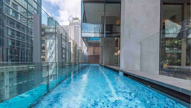 A modern indoor swimming pool with glass walls, surrounded by high-rise buildings.