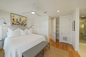 A bedroom with a large bed, a ceiling fan, a bench, and a glass shower area.