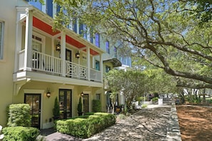 A two-story building with a balcony, a covered porch, and a pathway leading to a park.