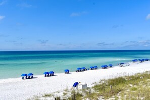 Ein Strand mit weißem Sand, klarem türkisblauem Wasser und blauen Sonnenschirmen.