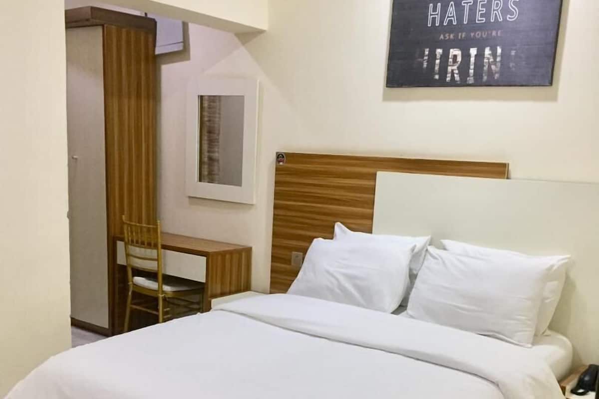 A neatly made bed with white linens, a wooden headboard, and a bedside table with a phone. A motivational quote is displayed on the wall.