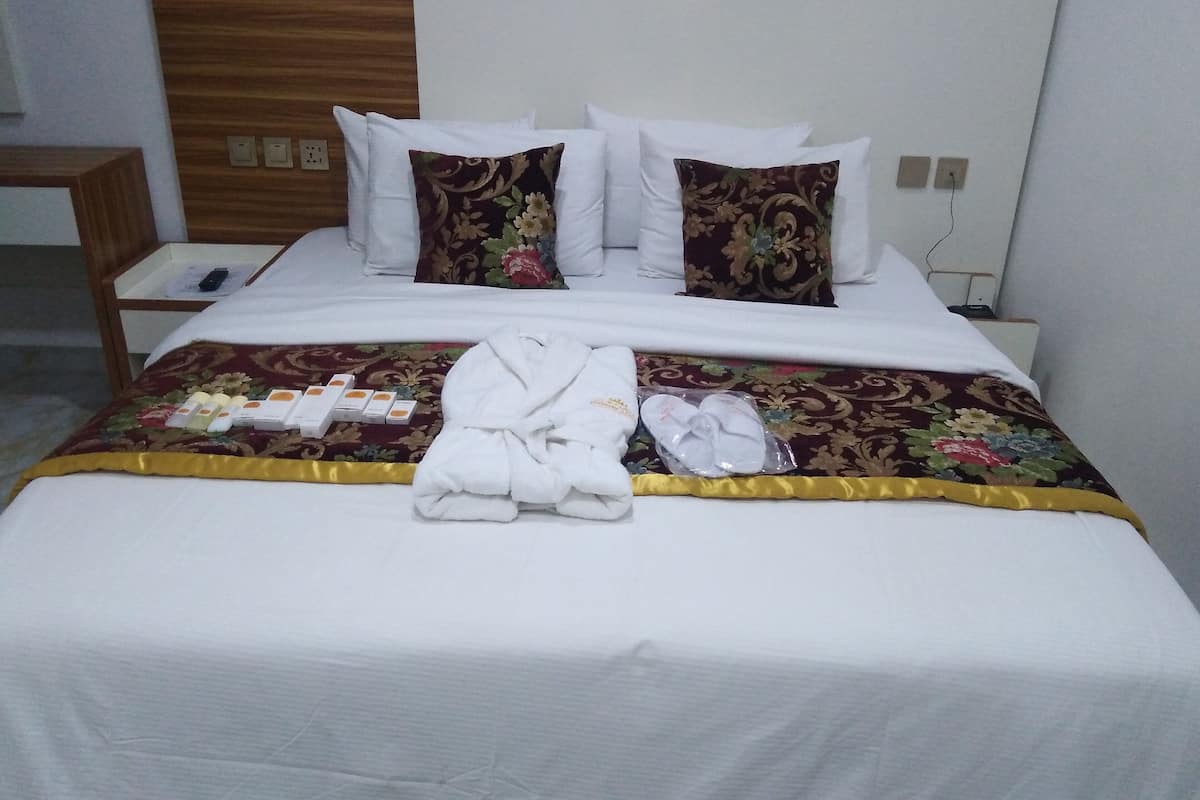 A neatly made bed with a floral-patterned bedspread, white pillows, and a white bathrobe and slippers on the bed.