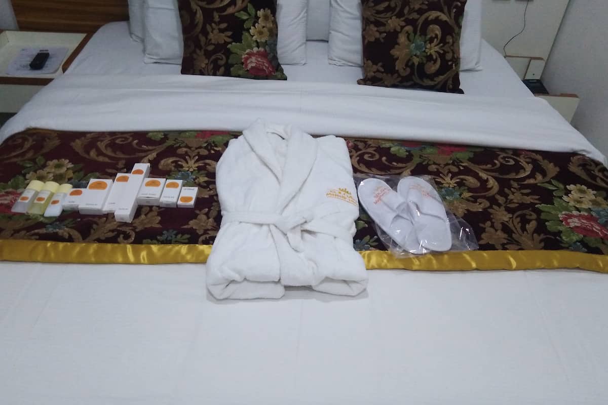 A neatly made bed with a floral-patterned bedspread, a white bathrobe, slippers, and toiletries on a hotel room.