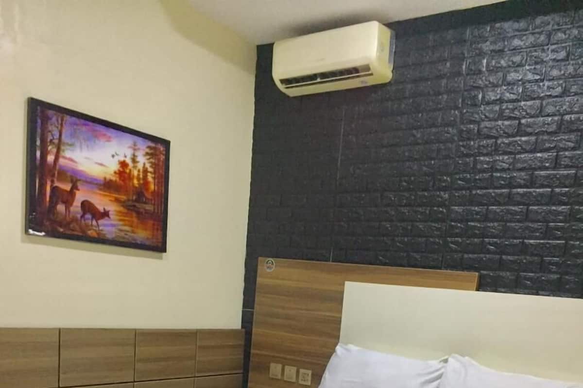 A hotel room with a bed, a painting on the wall, and an air conditioning unit.