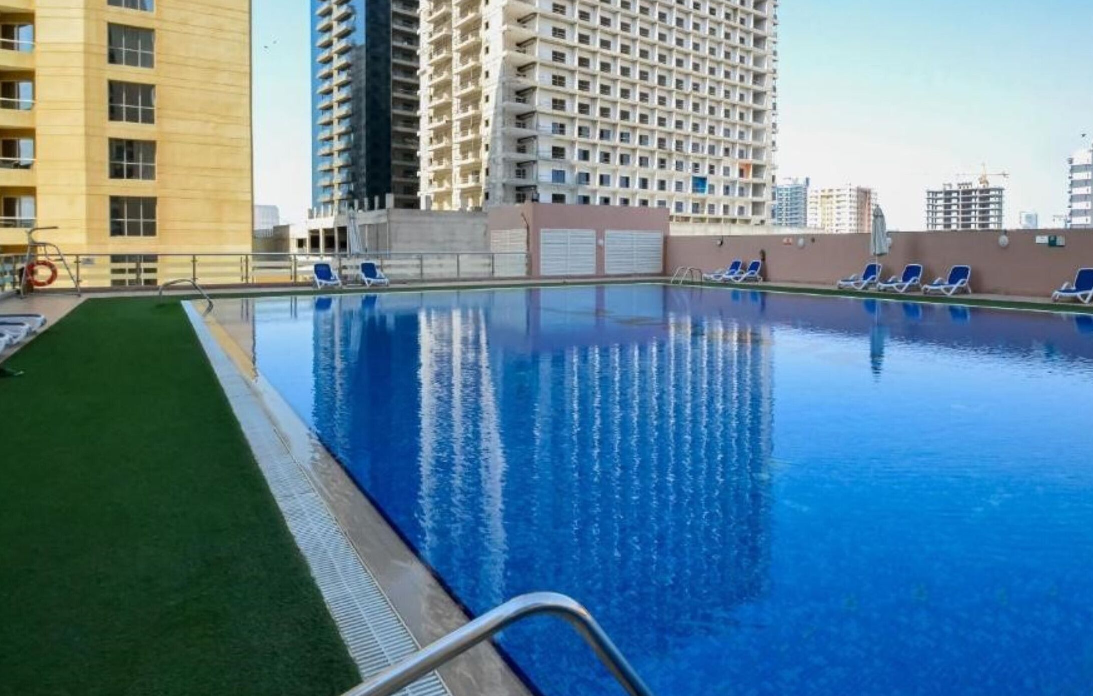 Una piscina con agua azul cristalina, rodeada de sillas de descanso y una zona verde.