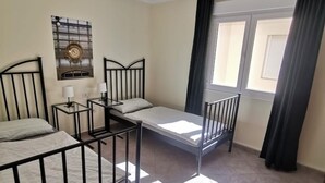 Una habitación con tres literas, dos mesitas de noche con lámparas, un reloj de pared y una ventana con cortinas.