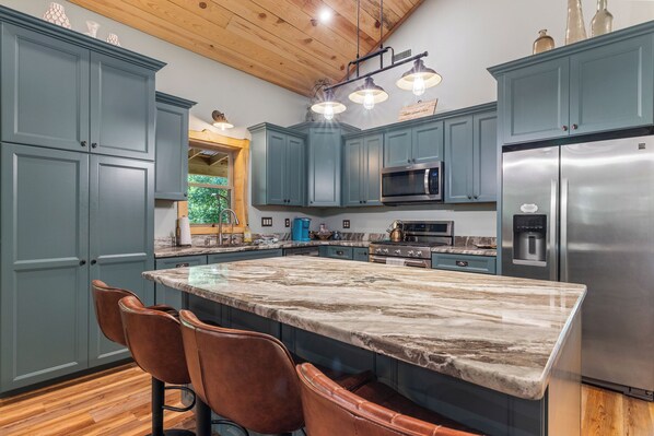 A modern kitchen with teal cabinets, a large marble island, and stainless steel appliances.