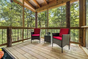 A wooden deck with two wicker chairs and a small table, surrounded by trees.