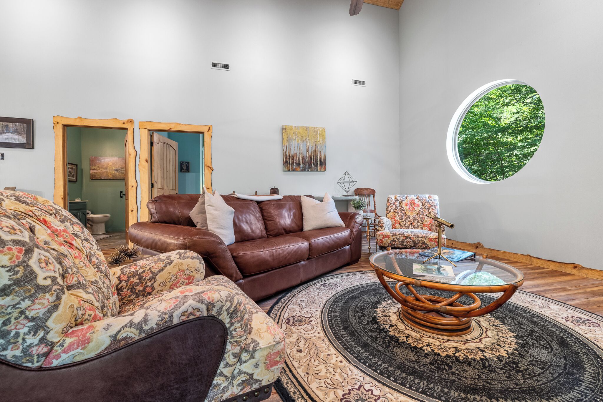 A modern living room with a brown leather sofa, a patterned armchair, and a round glass coffee table with a woven base.