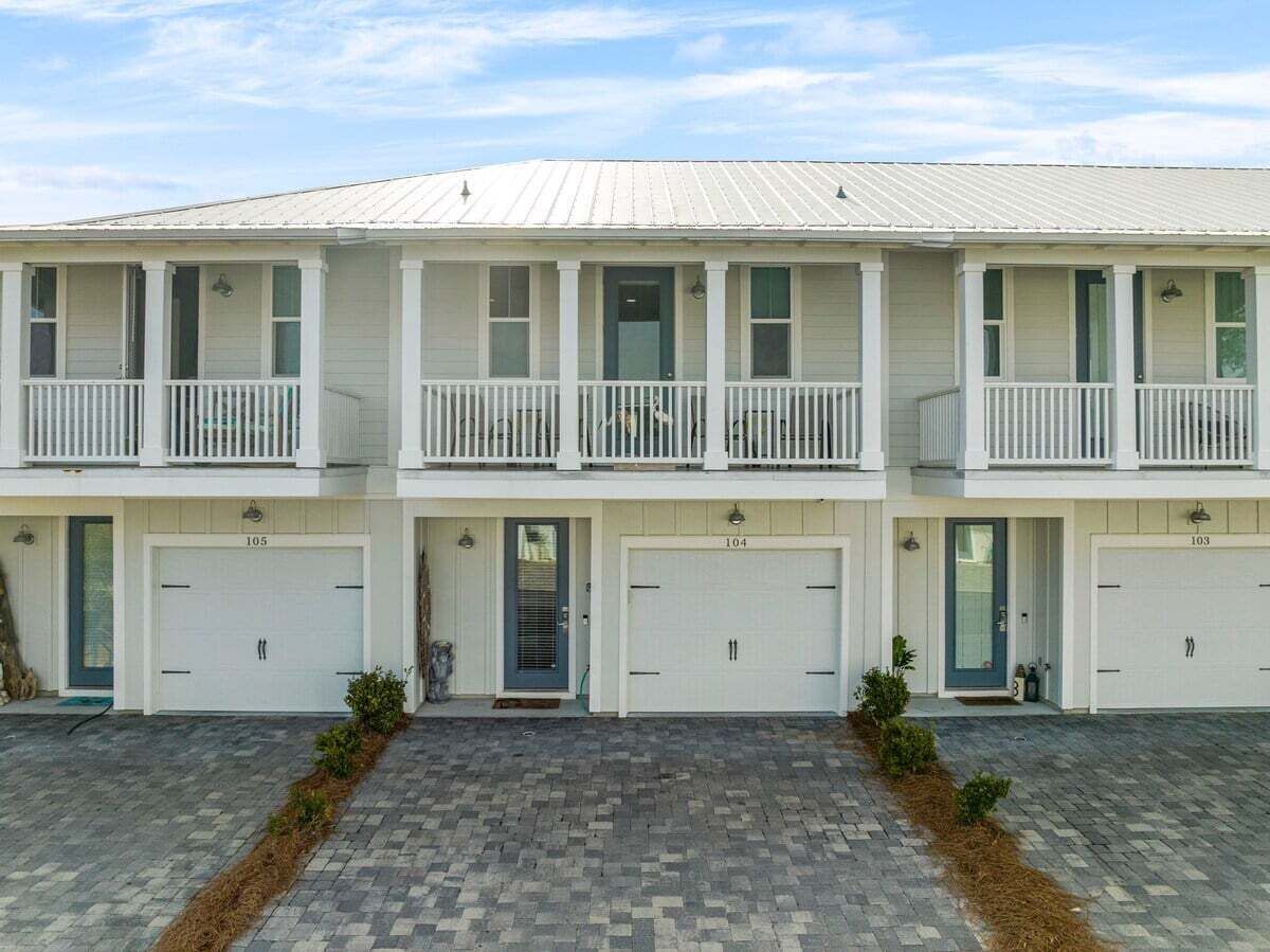 A two-story building with a white facade, a covered front porch, and three garage doors numbered 103, 104, and 105.