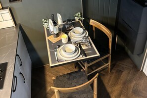 Una mesa de comedor dispuesta con platos, vasos y una botella, en una habitación con piso de madera y una silla.