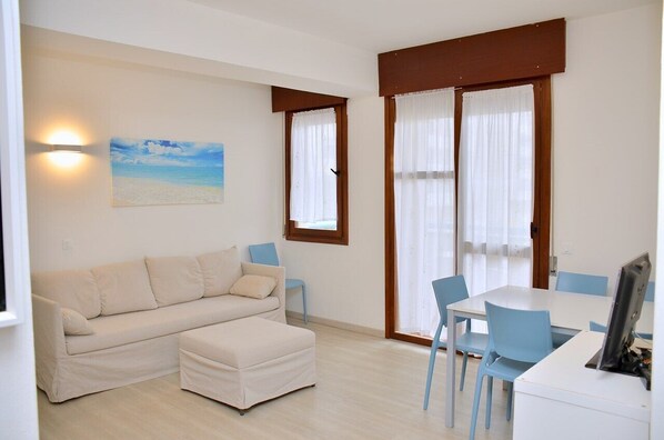 Une pièce comprenant un canapé, une table à manger et des chaises. Il y a un tableau au mur et une fenêtre avec des rideaux.