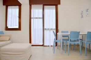 Une pièce comprenant un canapé, une table à manger avec des chaises et une fenêtre avec des rideaux.