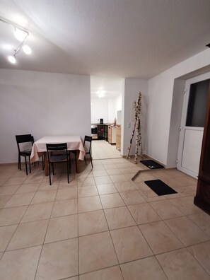 A spacious room with a dining table and chairs, a kitchen in the background, and a door with a window. - [r]auszeit, 65 qm Apartment, für Wanderlustige und Stadtbummler (Nittendorf)