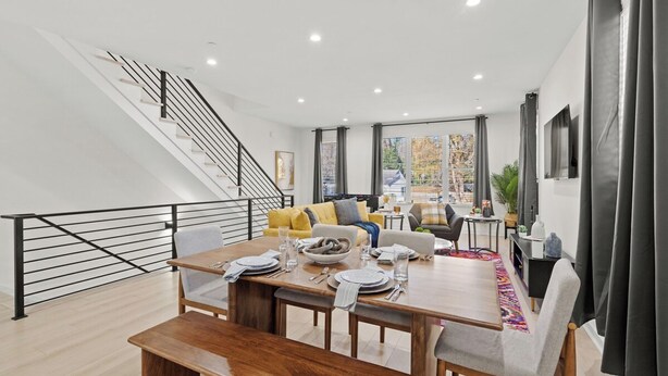 A modern dining area with a wooden table set for four, a staircase with a railing, and a living area with a sofa and a coffee table. - Stylish Stay with Rooftop Views and Garage Access (Charlotte)