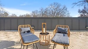A patio with two wicker chairs and a small table, a grey wall in the background, and trees. - Stylish Stay with Rooftop Views and Garage Access (Charlotte)