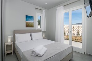 Une chambre à coucher avec un lit, une table de chevet, un téléviseur fixé au mur et une fenêtre avec des rideaux.