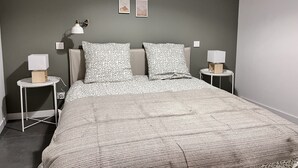 A neatly arranged bedroom with a bed, two bedside tables, a wall-mounted lamp, and framed pictures.