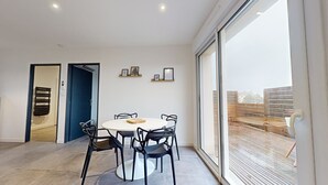 A modern dining area with a round table and chairs, a blue door, and a large window with a view of a wooden deck.