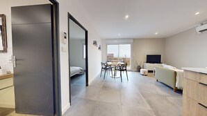 A modern apartment with a dining area, a sofa, a TV, and a kitchen.