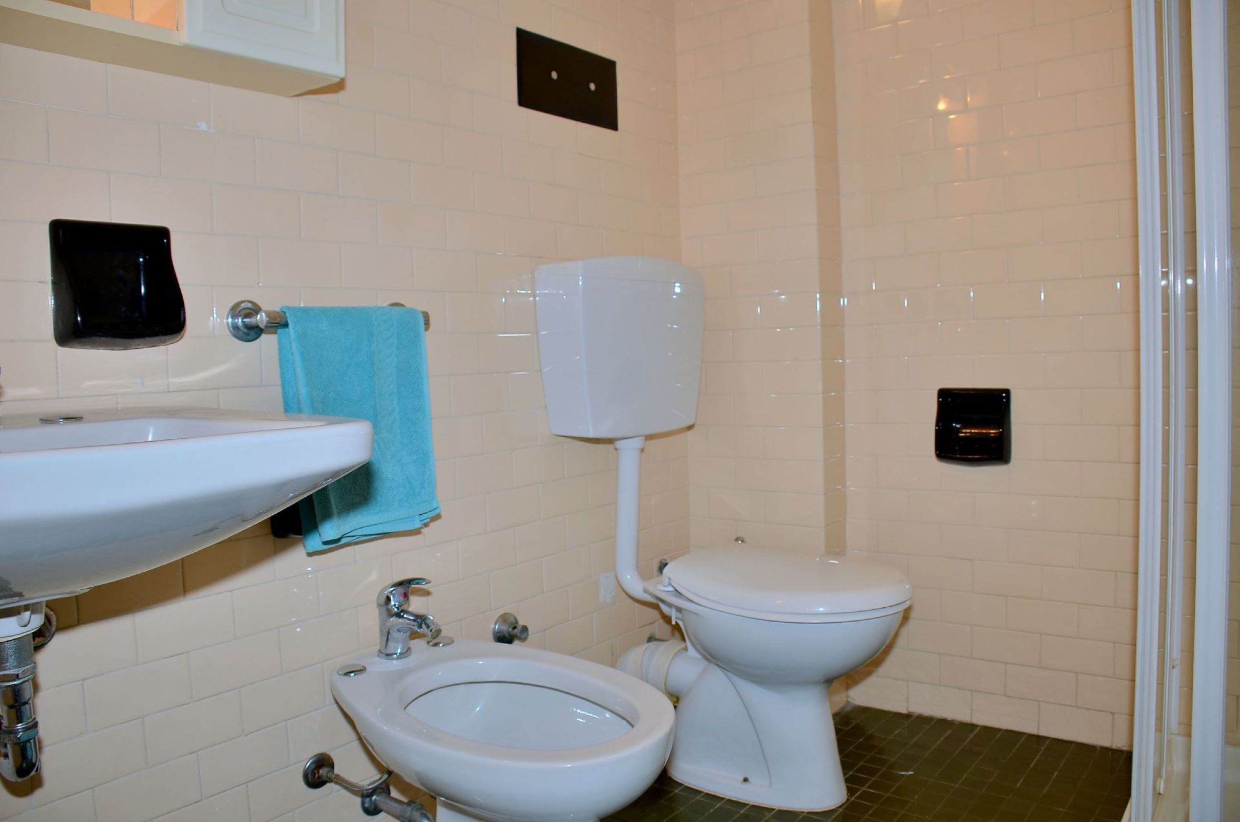 Un baño con lavamanos, bidé, inodoro y una toalla colgada en la pared.
