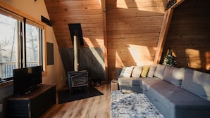 Una sala de estar acogedora con detalles de madera, un sofá, una televisión y una estufa de leña.