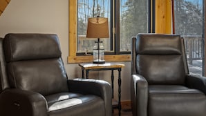 Dos sillones de cuero, una mesa con una lámpara y una ventana con vistas a árboles.