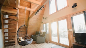 Un acogedor interior de cabaña con paredes de madera, un sillón colgante, un sofá y un televisor.