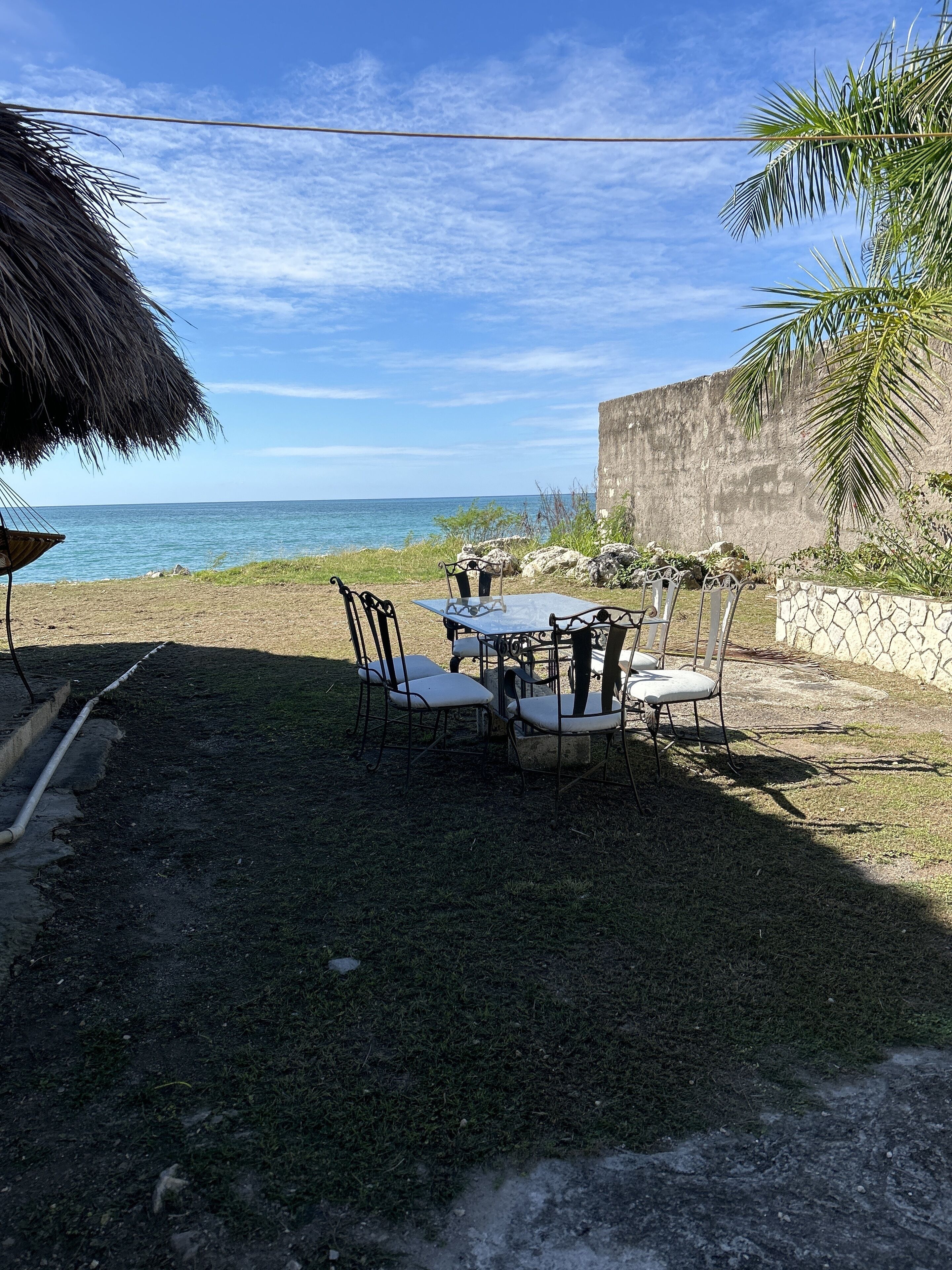 An outdoor dining area with a table and chairs, a thatched umbrella, and a view of the ocean.