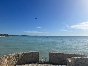 A stone wall with a metal railing overlooking a calm sea.