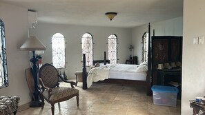 A bedroom with a large bed, a chair, a desk, and a window with a view.