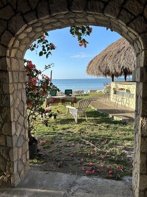 An outdoor seating area with stone walls, a thatched roof, and a view of the sea. - The Belair (Bluefields)