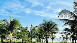 A pathway leading through a well-maintained garden with palm trees and a clear blue sky. - Cam Ranh Beach Resort near The Airport (Bac Cam Ranh)