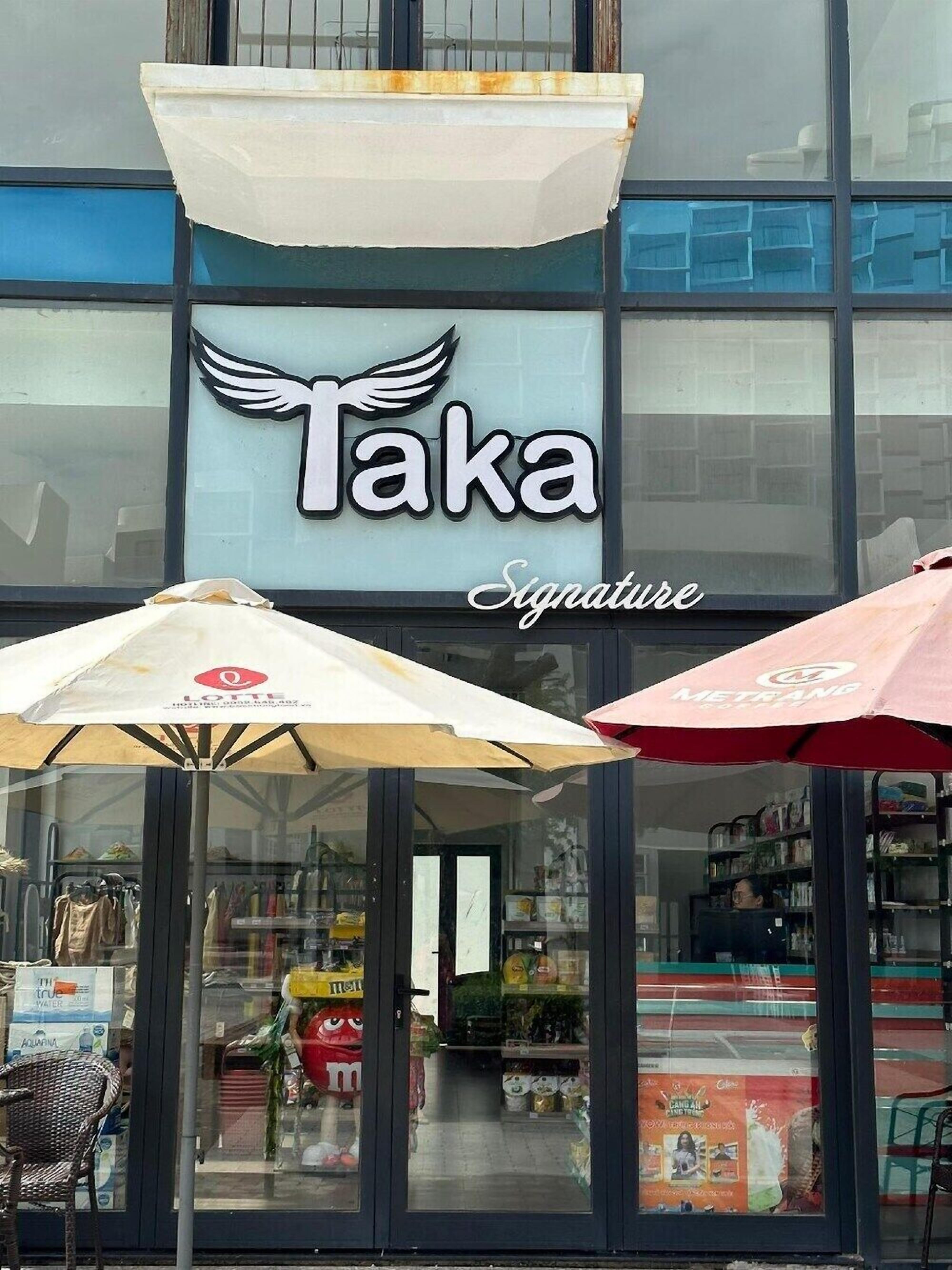 A storefront with a sign reading 'Taka Signature' and two umbrellas in front.