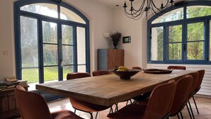 A dining area with a large wooden table, six brown chairs, and a chandelier.