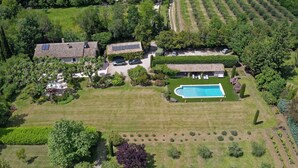 An aerial view of a residential property with a swimming pool, multiple houses, and well-maintained gardens.