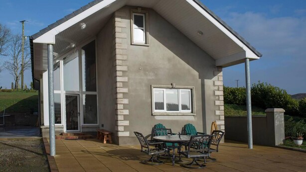 Une maison moderne dotée d’une grande porte vitrée, d’un patio avec des meubles d’extérieur et d’un ciel dégagé.