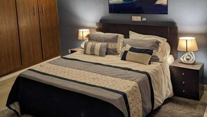 A bedroom with a large bed, wooden wardrobe, and a painting on the wall. - APPARTEMENTS 2 PIECES BELLE RIVE  (Abidjan)