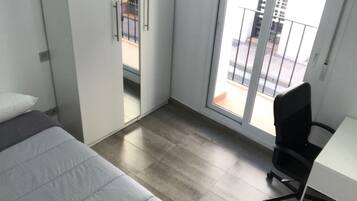 Habitación de hotel moderna con cama, escritorio y silla. Posee una puerta corrediza de vidrio que da a un balcón con vistas a la ciudad.